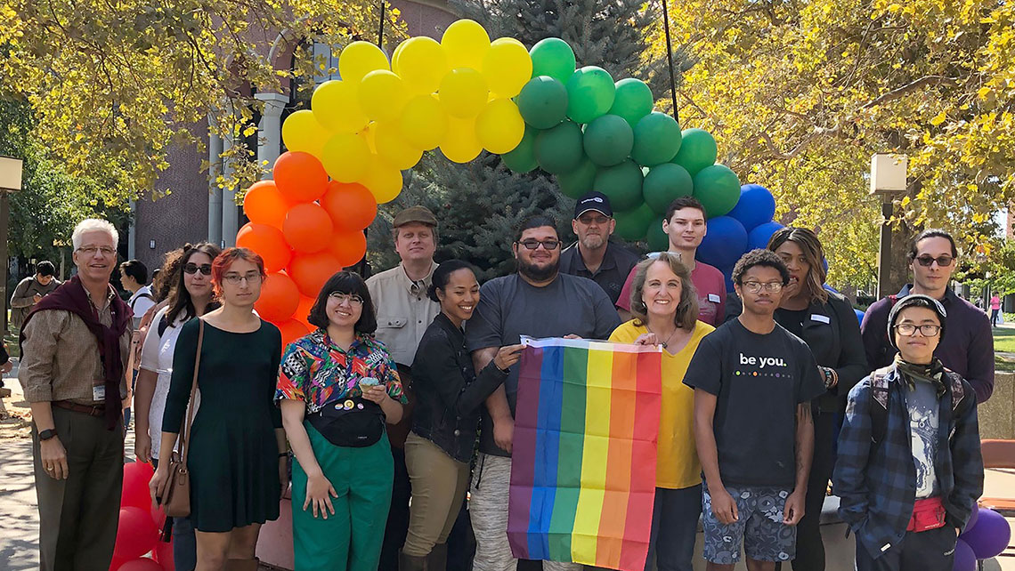 National Coming Out Day group photo with rainbow balloon arch
