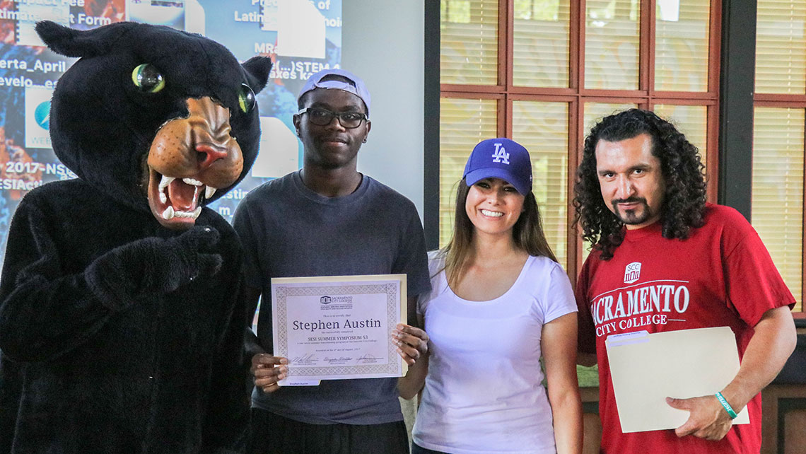 Stephen holding a SESI certificate and surrounded by staff and the SCC panther mascot