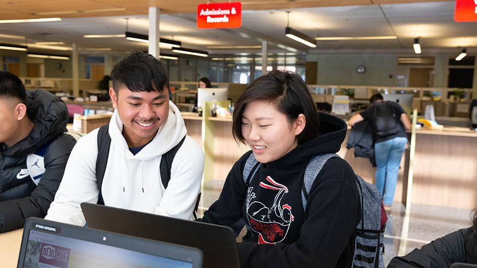 Two students at a laptop, smiling